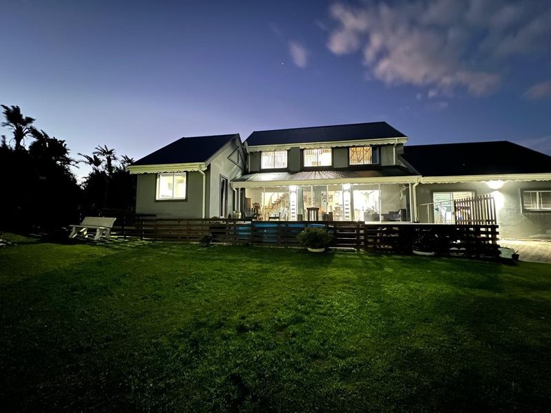 Rear exterior view of the house at dusk, featuring a swimming pool, timber decking, and a well-maintained lawn area.