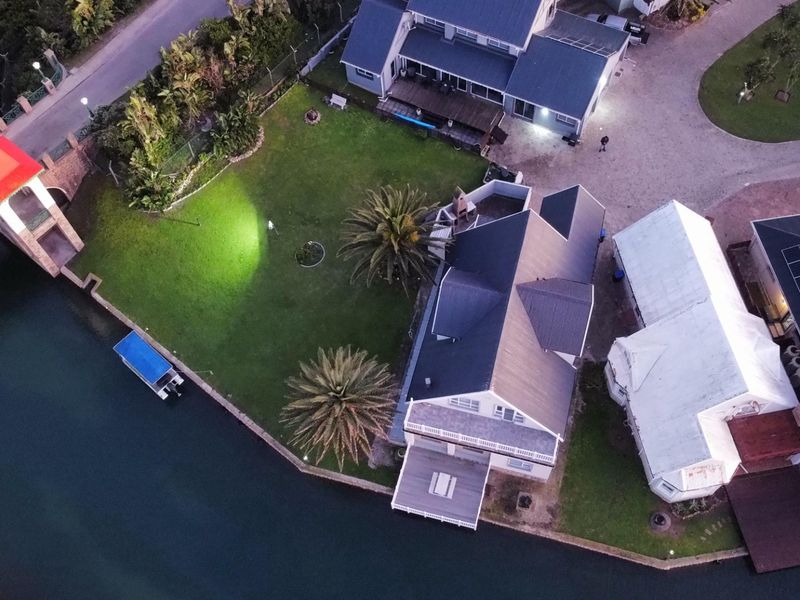 Aerial view of a waterfront property featuring a large garden, paved driveway, multiple roof structures with solar panels, and direct canal access.