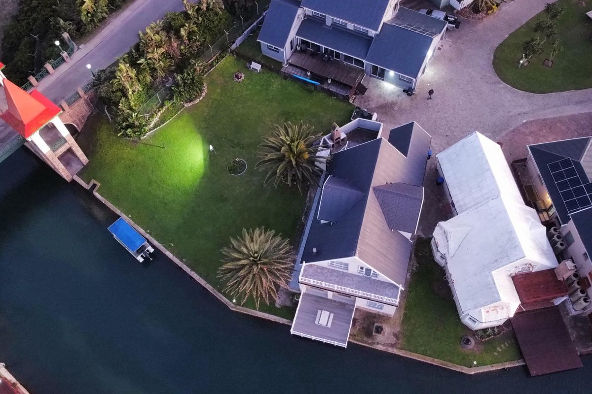 Aerial view of a waterfront property featuring a large garden, paved driveway, multiple roof structures with solar panels, and direct canal access.