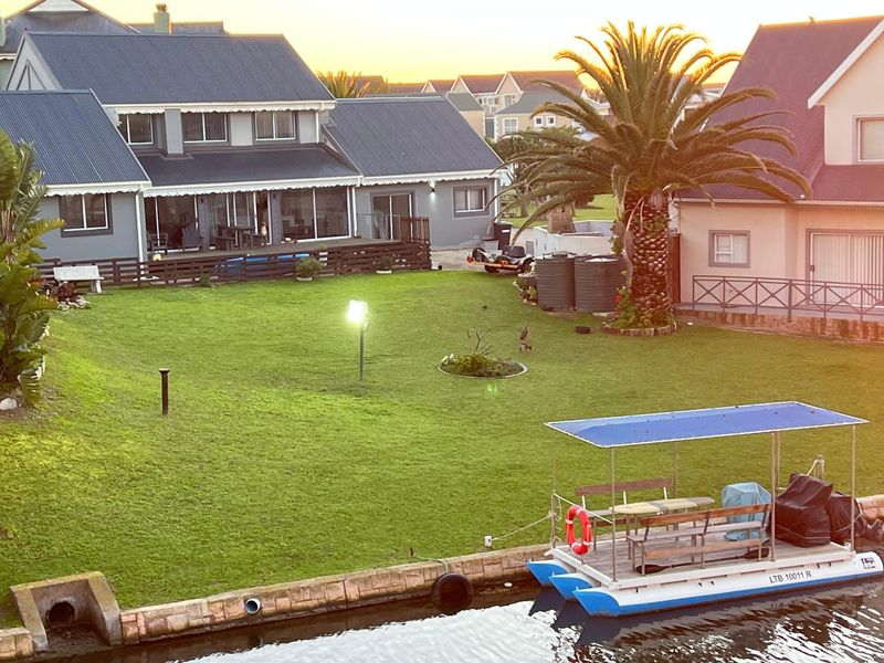 Rear view of the property featuring a spacious lawn, timber decking, and direct access to the canal with a private mooring area.