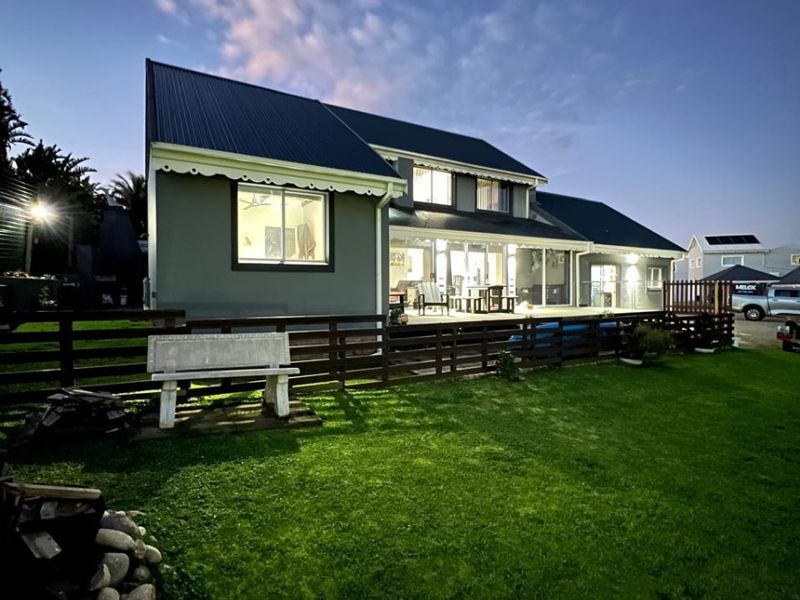 Rear view of the property featuring a spacious timber deck, well-maintained lawn, and metal roofing at twilight.