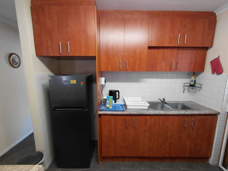 A functional kitchen featuring wood-look laminate cabinetry, a double bowl stainless steel sink, and a tiled splashback, offering a practical layout for daily use.