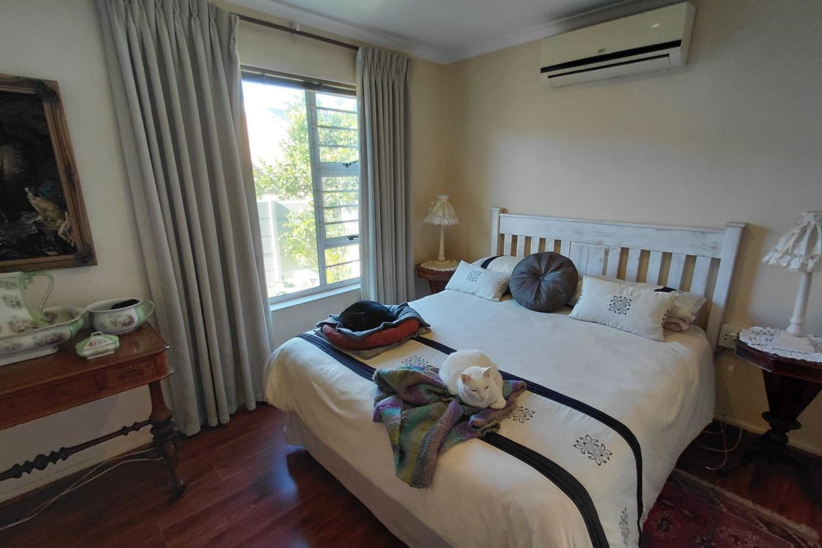 A well-lit bedroom featuring laminate flooring, a wall-mounted split-system air conditioner, and large windows with curtains.