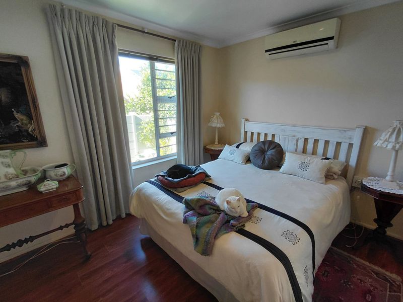 A well-lit bedroom featuring laminate flooring, a wall-mounted split-system air conditioner, and large windows with curtains.
