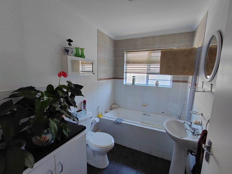 A functional bathroom featuring a pedestal basin, toilet, and a bathtub with tiled splashbacks and a window for natural light.