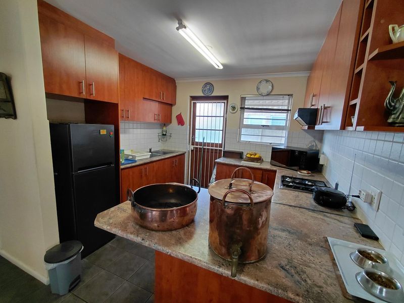 A functional kitchen featuring wood-finish cabinetry, stone countertops, a gas hob with extractor, and a tiled backsplash, with direct access to the exterior.