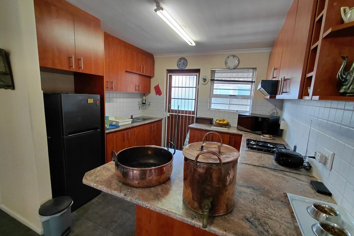 A functional kitchen featuring wood-finish cabinetry, stone countertops, a gas hob with extractor, and a tiled backsplash, with direct access to the exterior.