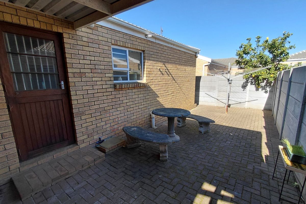 A paved rear courtyard area featuring face brick walls, a covered patio section, and a precast concrete boundary wall.