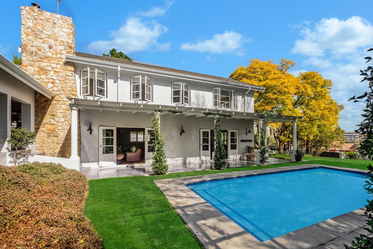 Rear view of the property featuring a covered patio, stone chimney, and a well-maintained swimming pool set within a landscaped garden.