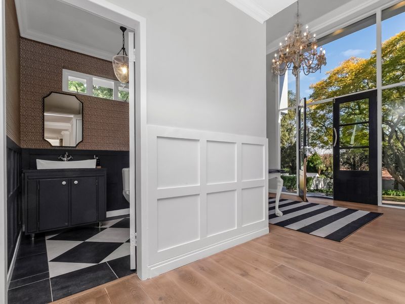Elegant entrance hall featuring timber flooring, wainscoting, and a modern guest bathroom with a vessel sink and patterned tile flooring.