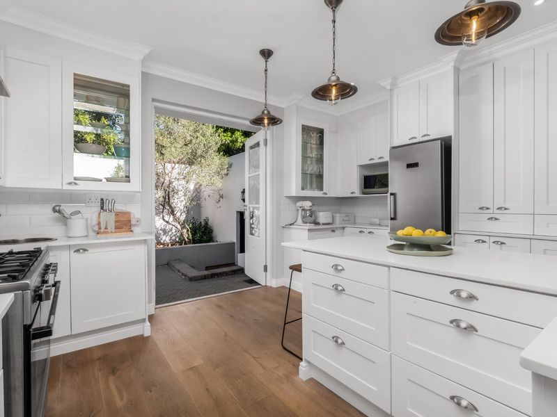 Modern white kitchen featuring shaker-style cabinetry, quartz countertops, a central island, gas stove, and direct access to a private outdoor courtyard.