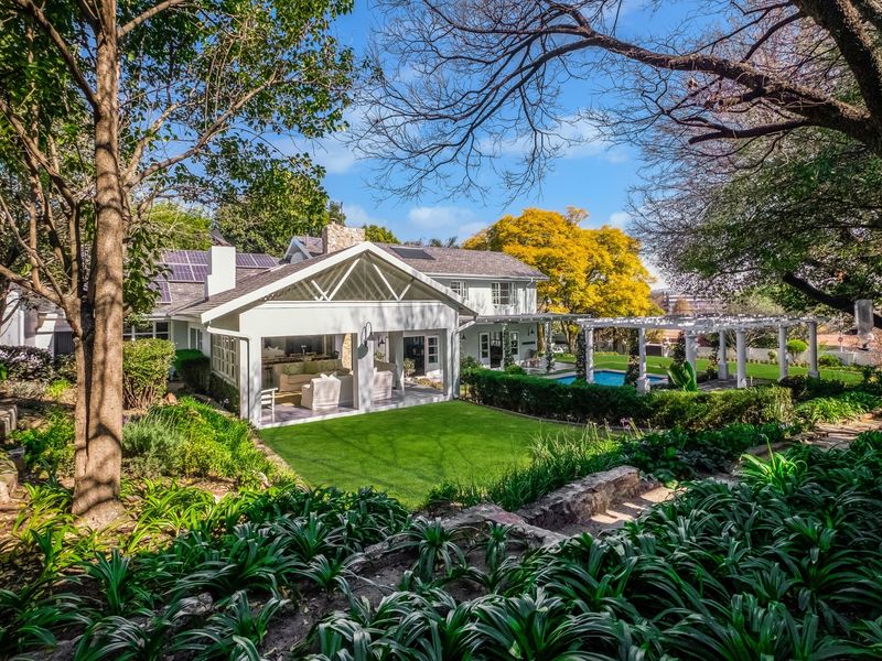 A beautifully landscaped rear garden featuring a swimming pool, a white pergola, and a spacious covered patio attached to the main residence.