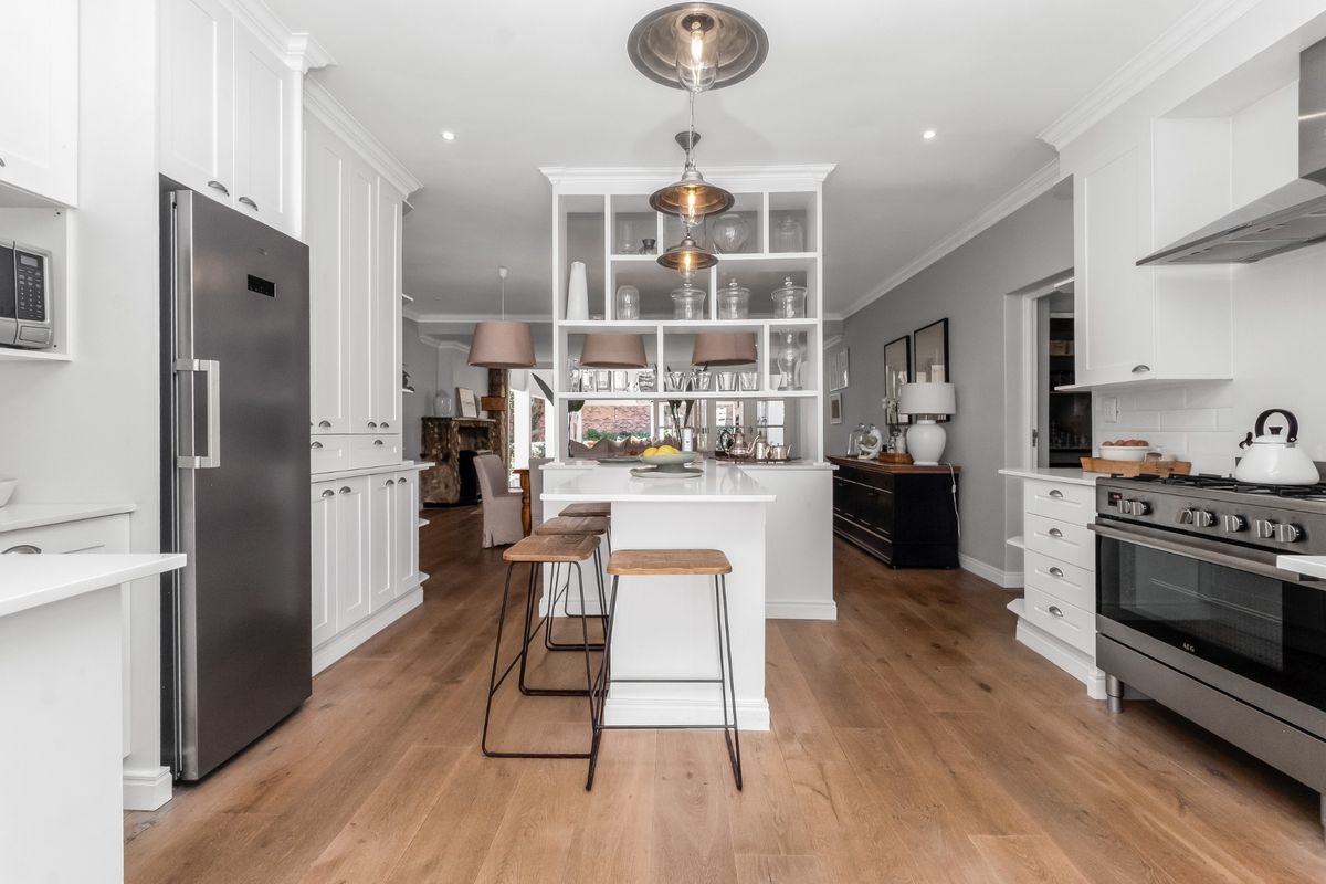 Modern kitchen featuring white cabinetry, a central island with open shelving, stainless steel appliances, and warm hardwood flooring, seamlessly flowing into the living area.