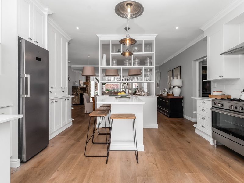 Modern kitchen featuring white cabinetry, a central island with open shelving, stainless steel appliances, and warm hardwood flooring, seamlessly flowing into the living area.
