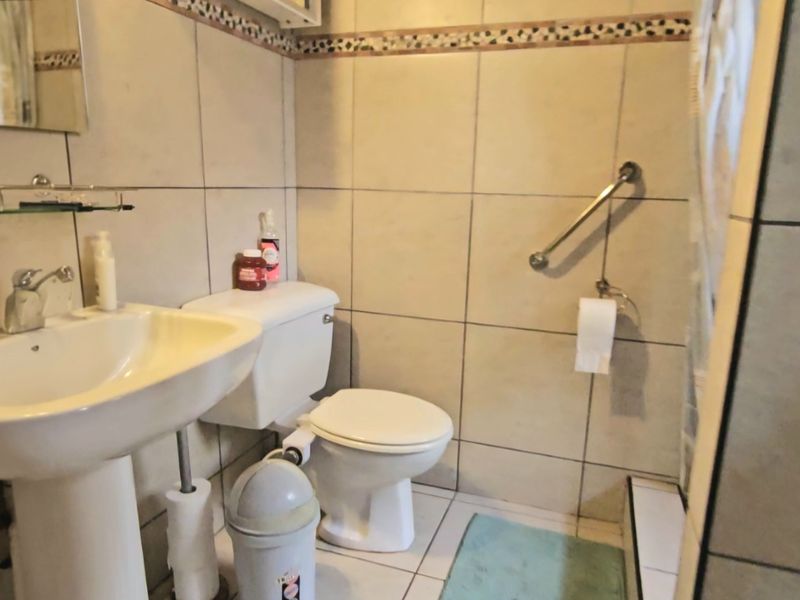 A functional bathroom featuring a pedestal basin, toilet, and wall-mounted grab rail, finished with neutral wall and floor tiles.