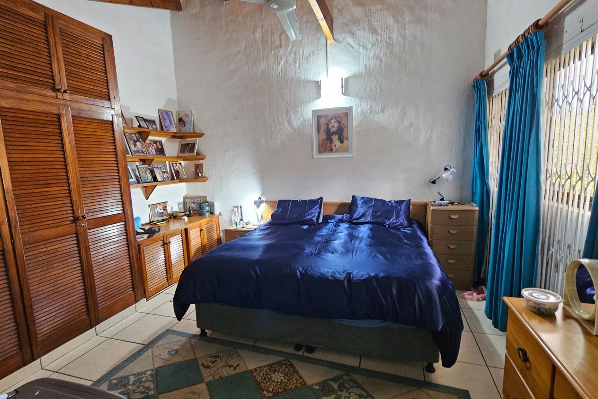 Spacious bedroom featuring built-in wooden cabinetry, exposed timber ceiling beams, and tiled flooring with access to a window secured by a metal gate.