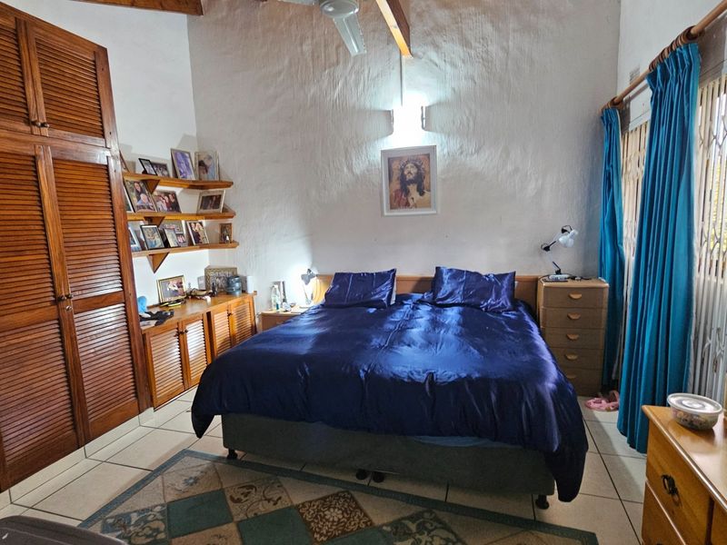 Spacious bedroom featuring built-in wooden cabinetry, exposed timber ceiling beams, and tiled flooring with access to a window secured by a metal gate.