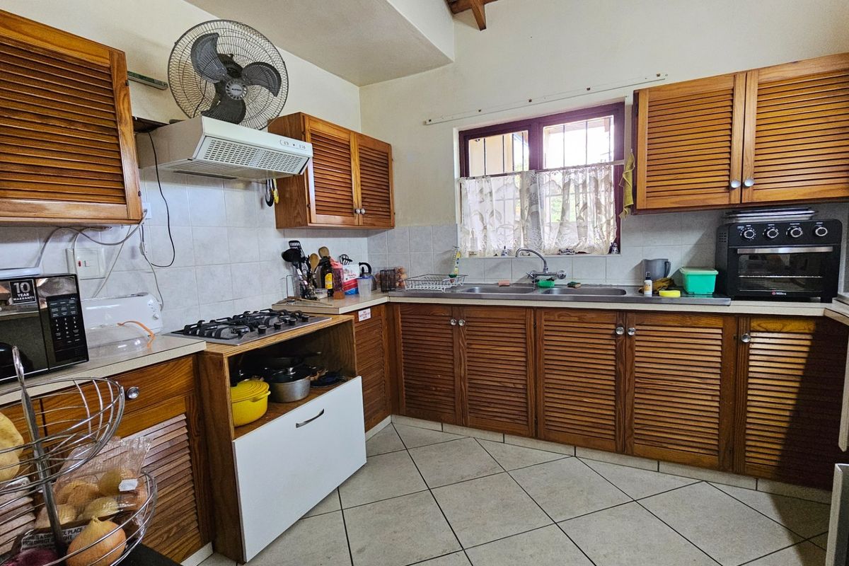A functional kitchen featuring louvered timber cabinetry, a gas hob with extractor fan, and a double bowl stainless steel sink with tiled splashback.