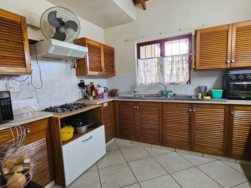 A functional kitchen featuring louvered timber cabinetry, a gas hob with extractor fan, and a double bowl stainless steel sink with tiled splashback.