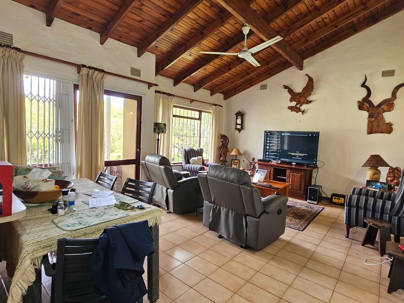 Spacious open-plan living and dining area featuring high exposed timber beam ceilings, tiled flooring, and direct access to the outdoors through sliding glass doors.