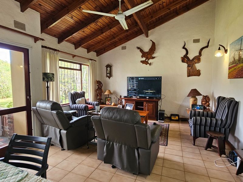 Spacious living room featuring a high vaulted timber ceiling, tiled flooring, and large windows with security bars, providing access to the outdoor area.