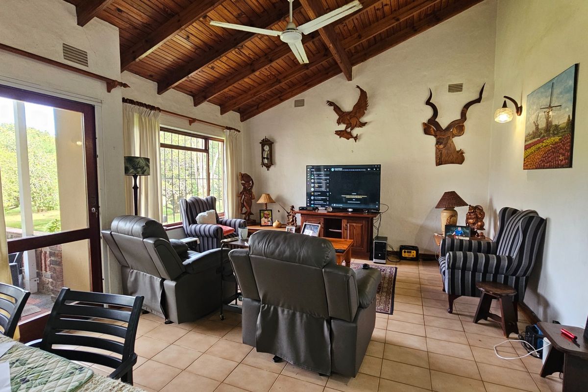 Spacious living room featuring a high vaulted timber ceiling, tiled flooring, and large windows with security bars, providing access to the outdoor area.
