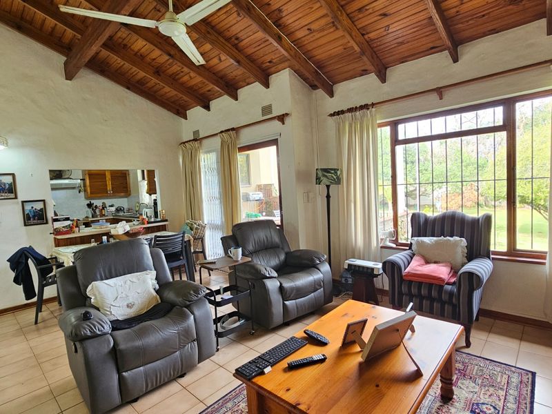Open-plan living area featuring a high exposed timber beam ceiling, tiled flooring, and a pass-through window connecting to the kitchen.