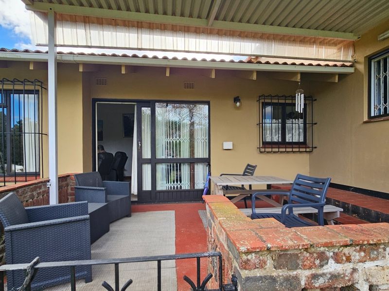 A covered outdoor patio area featuring brick wall accents, tiled flooring, and security bars on windows, providing a functional space for outdoor living.
