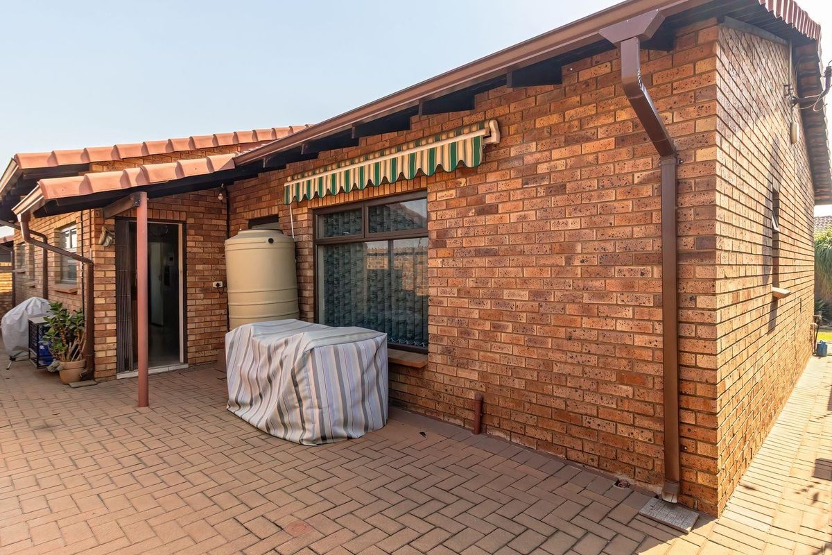 Rear exterior view of the house featuring a brick facade, paved patio area, water tank, and a retractable awning over the window.