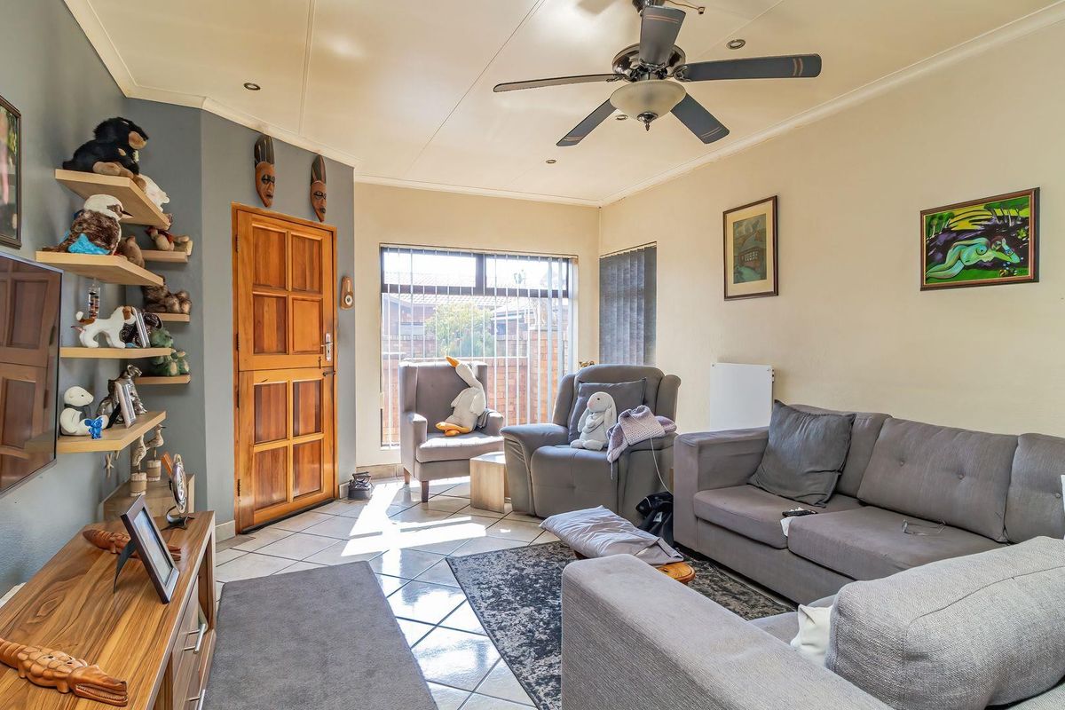 A comfortable living room featuring tiled flooring, a ceiling fan, and a timber entrance door, providing a functional and well-lit space.
