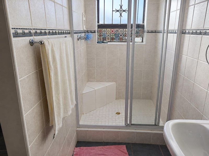 A functional bathroom featuring a tiled shower enclosure with a built-in corner seat and a window with security bars.