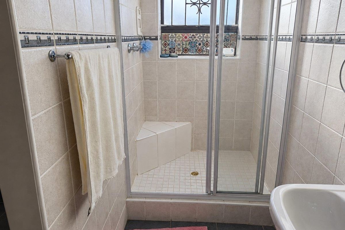 A functional bathroom featuring a tiled shower enclosure with a built-in corner seat and a window with security bars.