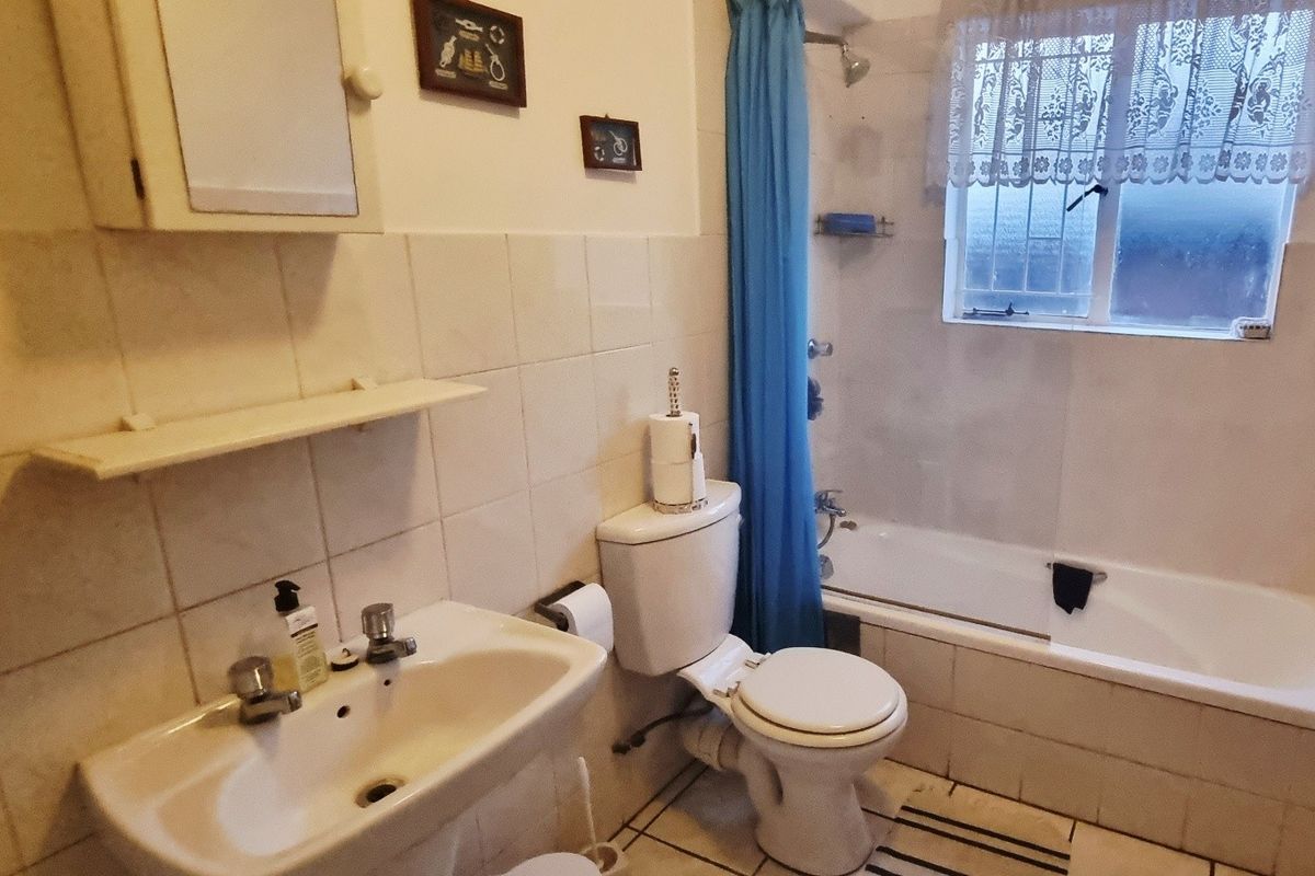 A functional bathroom featuring a bathtub with shower attachment, pedestal basin, and toilet, finished with neutral wall and floor tiles.