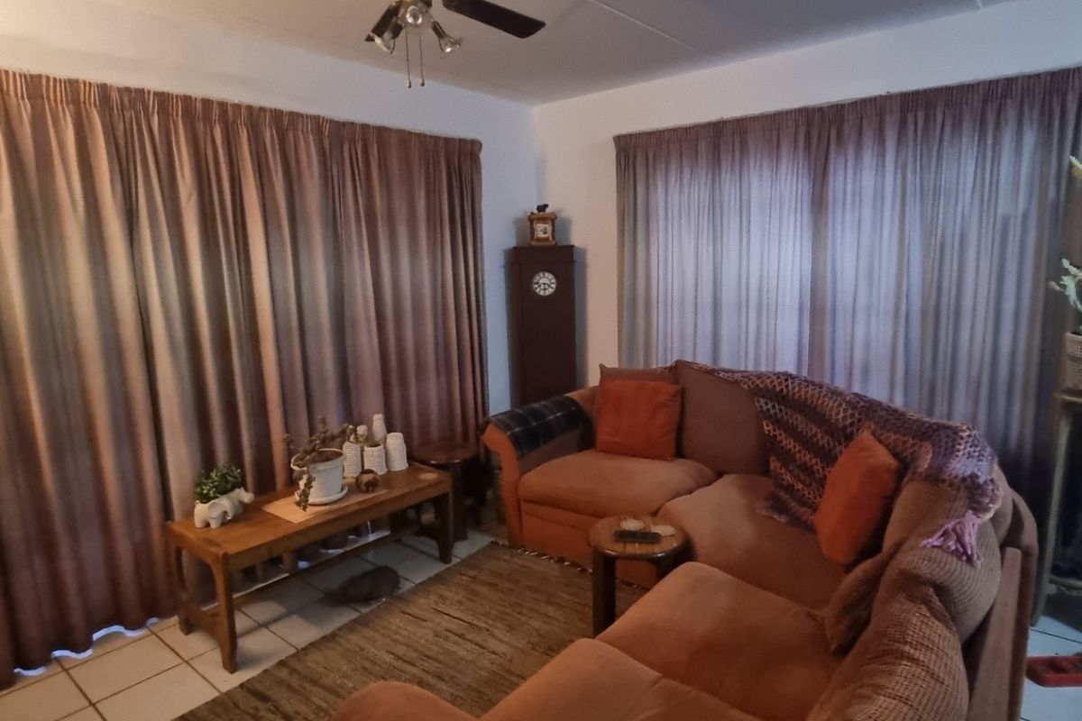 A living room area featuring tiled flooring and a ceiling fan, with large windows covered by full-length curtains.