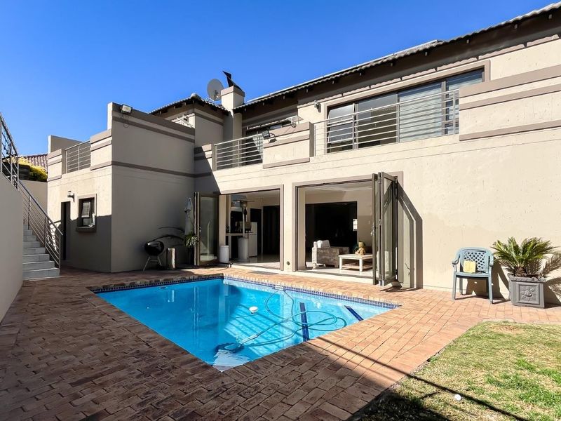 Rear exterior view featuring a swimming pool, paved patio area, and a multi-level structure with balcony access and large sliding doors.