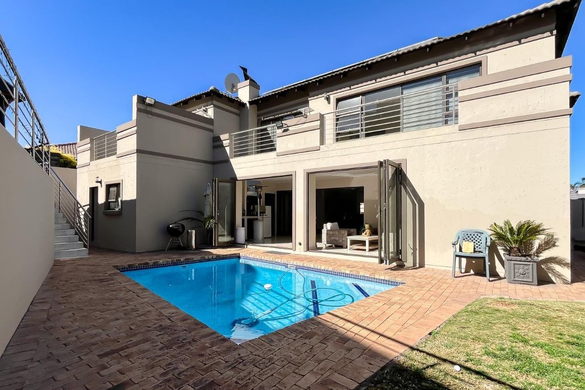 Rear exterior view featuring a swimming pool, paved patio area, and a multi-level structure with balcony access and large sliding doors.