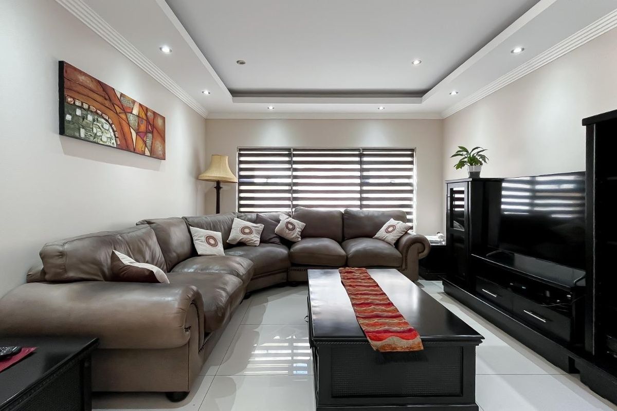 A well-maintained living room featuring a recessed ceiling with downlights, tiled flooring, and modern roller blinds.