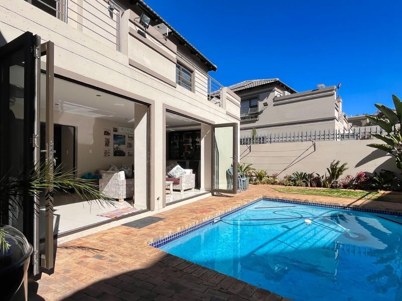 Rear exterior view featuring a swimming pool, brick-paved patio, and seamless indoor-outdoor flow through large bi-fold doors into the living area.