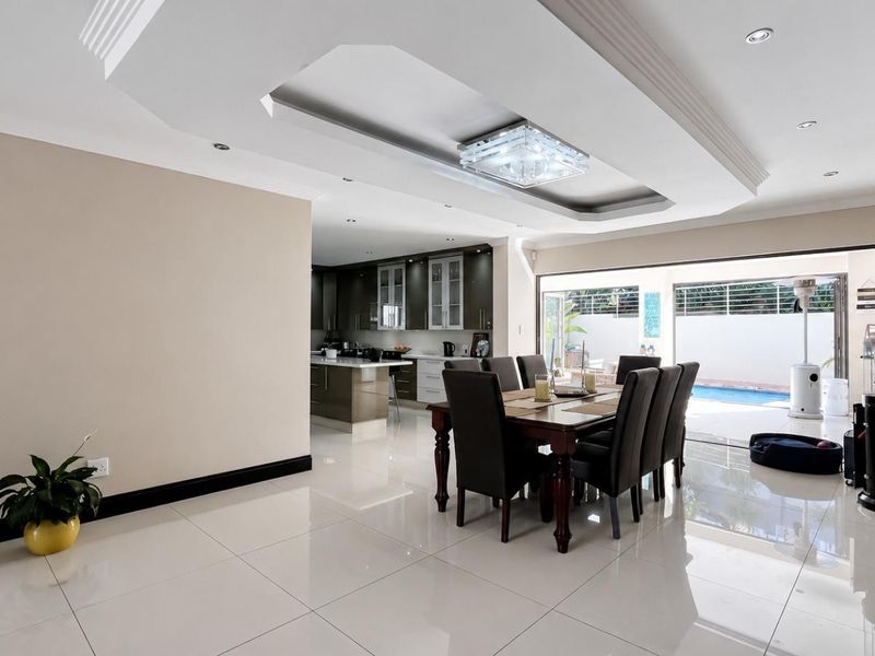 Spacious open-plan living and dining area featuring tiled floors, a recessed ceiling with modern lighting, and seamless flow to the outdoor pool area.