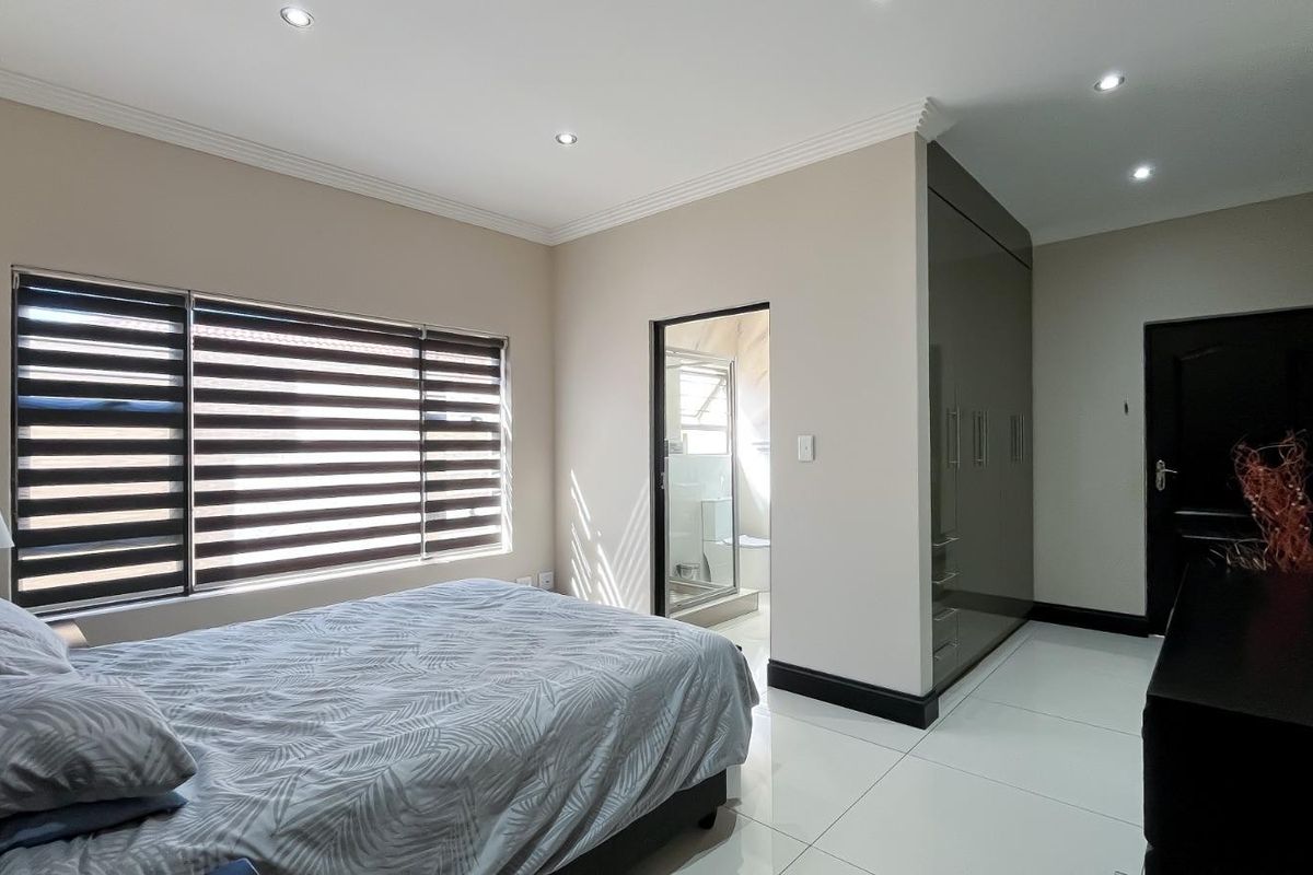 A modern bedroom featuring tiled flooring, recessed downlights, built-in cupboards, and an en-suite bathroom.