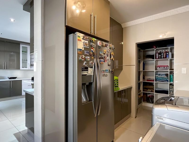 Modern kitchen featuring high-gloss cabinetry, stone countertops, integrated storage, and a convenient walk-in pantry area with tiled flooring throughout.