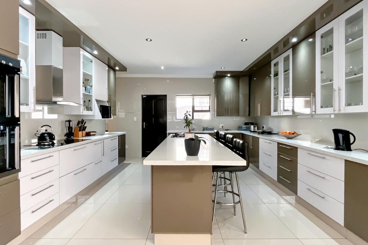 Modern, spacious kitchen featuring high-gloss cabinetry, a central island with stone countertops, integrated appliances, and sleek tiled flooring.