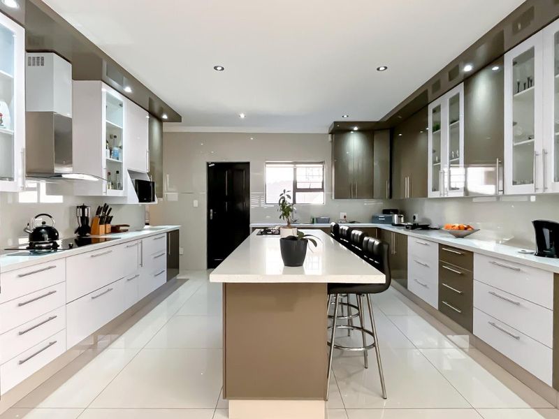 Modern, spacious kitchen featuring high-gloss cabinetry, a central island with stone countertops, integrated appliances, and sleek tiled flooring.