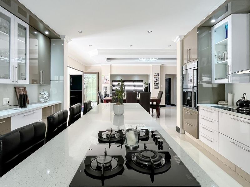 Modern open-plan kitchen featuring a large central island with gas cooktop, sleek gloss cabinetry, stone countertops, and integrated appliances, flowing into the dining area.