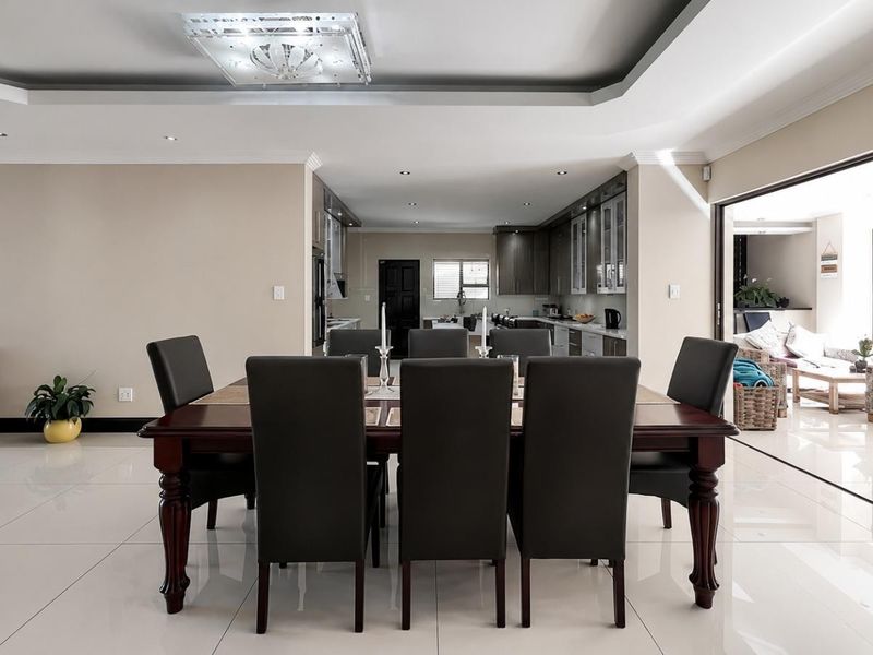 Spacious open-plan dining and kitchen area featuring modern porcelain tiles, recessed ceiling lighting, and seamless access to an outdoor patio through large sliding doors.