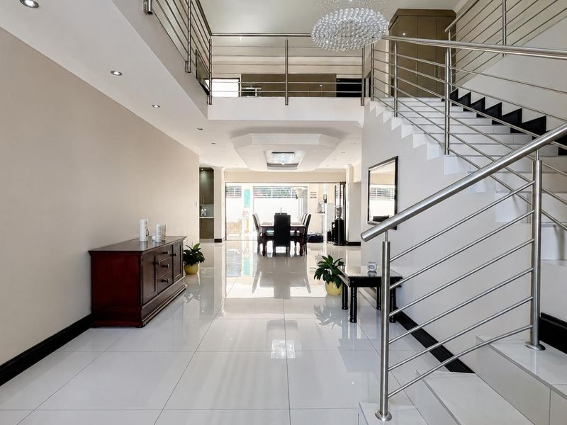 Spacious double-volume entrance hall featuring polished tiled flooring, a modern stainless steel staircase, and an elegant mezzanine landing overlooking the living area.