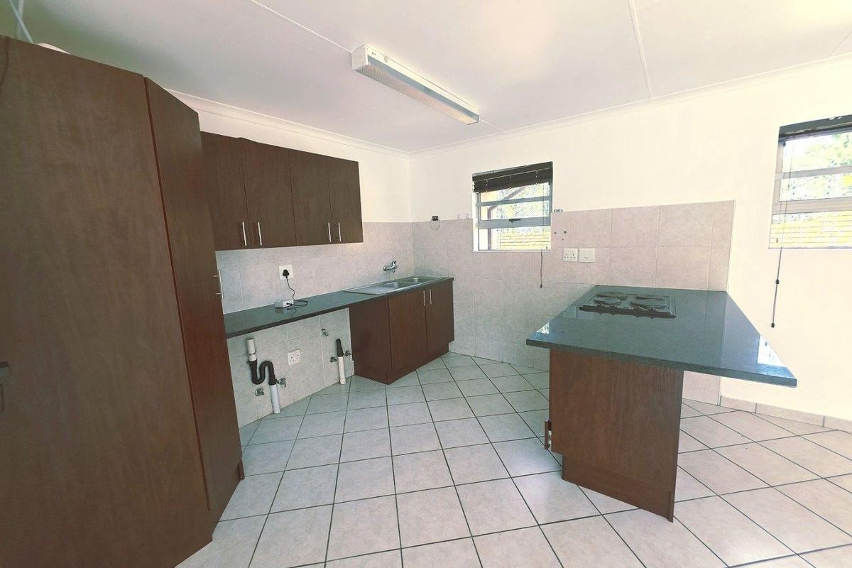 A functional kitchen featuring dark wood cabinetry, tiled flooring, a gas hob, and a stainless steel sink with exposed plumbing.