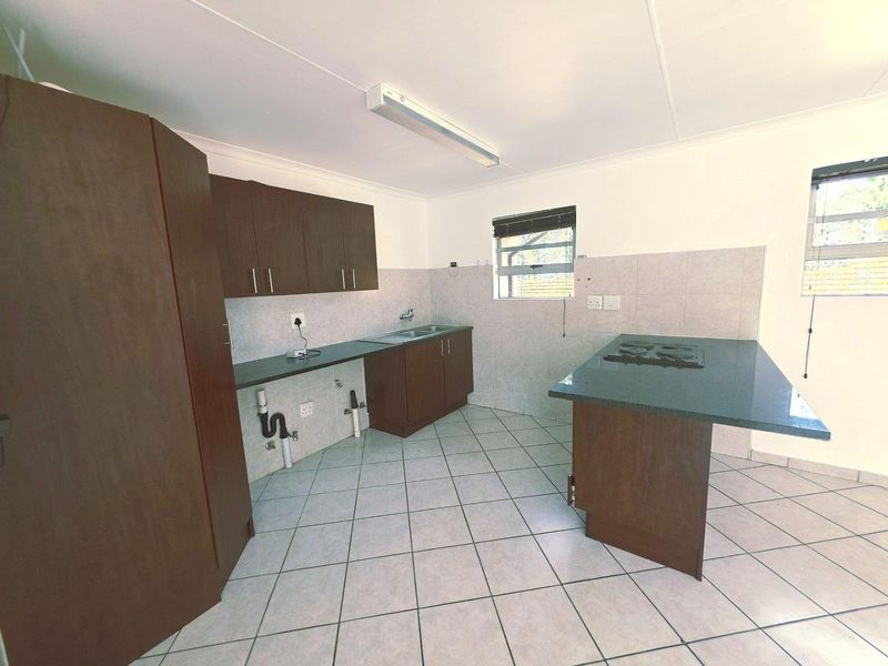 A functional kitchen featuring dark wood cabinetry, tiled flooring, a gas hob, and a stainless steel sink with exposed plumbing.