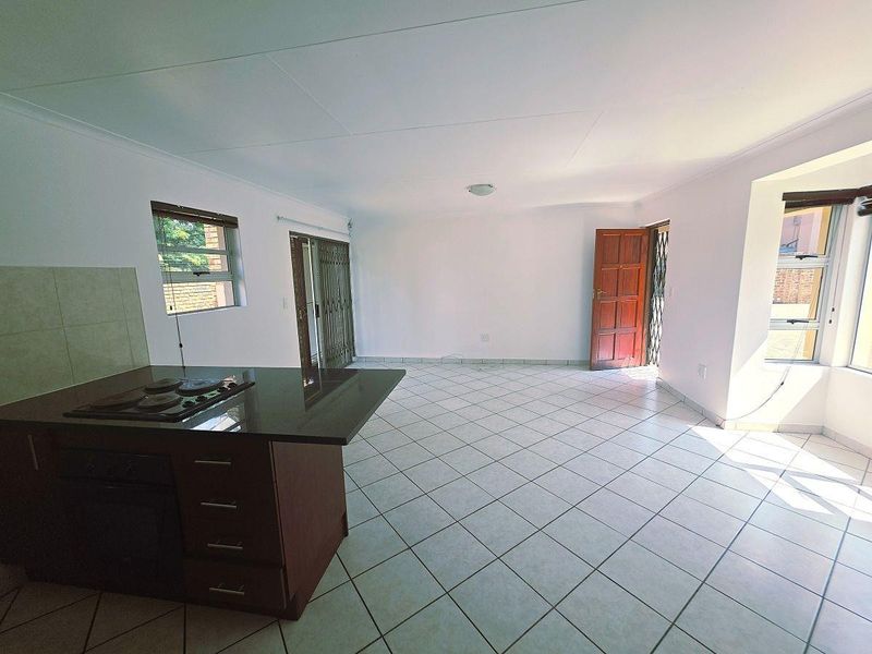 Spacious open-plan living area featuring a kitchen island with built-in hob and oven, tiled flooring, and direct access to the exterior.