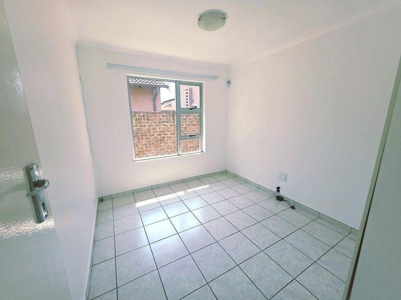A clean, empty bedroom featuring neutral tiled flooring, white walls, and an aluminium-framed window providing natural light.